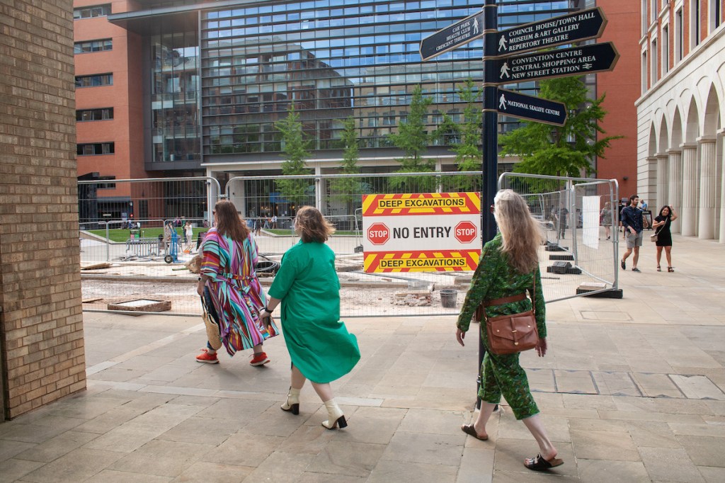 Three crones walking at Brindleyplace Birmingham. A sign says Deep Excavations.