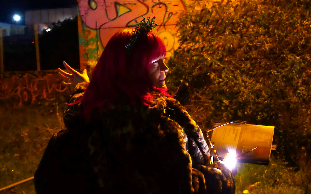 A white woman with pink hair lit by streetlights in an urban setting