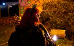 A white woman with pink hair lit by streetlights in an urban setting