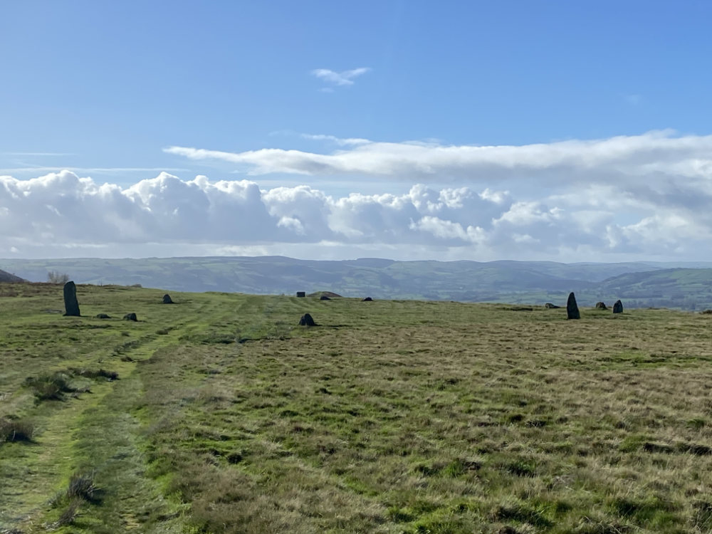 Mitchell's Fold stone circle from a distance, on a summer's day with white clouds and blue sky